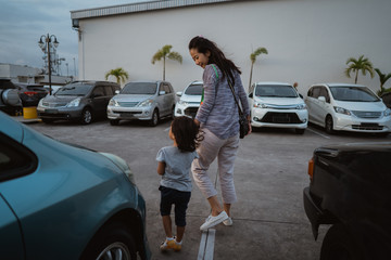 portrait of young asian woman with a little girl walking leaves parking car area