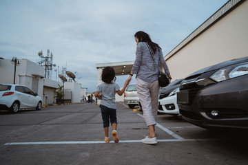 portrait of the mother holding her little daughter hand while walking between the car parks © Odua Images