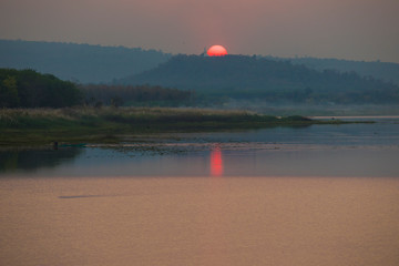 Big sun and mist in sunset with a Buddha statue on the mountain,The sunset at the back of the Buddha on the high mountain,Beautiful big orange sunset