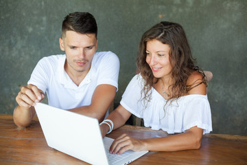 love, family, technology, internet and happiness concept - smiling happy couple with laptop computer at the desk, interior, indoor
