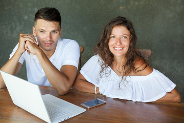 love, family, technology, internet and happiness concept - smiling happy couple with laptop computer at the desk, interior, indoor. Girl looks at the camera