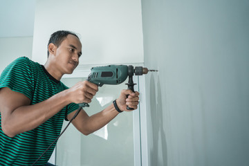 portrait of young man used a drill on the wall in the office room