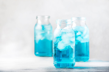 Sport and fitness drink concept, cold isotonic blue water in bottles, gray table background, selective focus