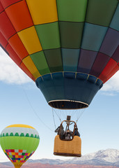 Fototapeta premium Three people lift off in the basket of a colorful hot air balloon, one woman looks back and takes a picture with her cell phone.
