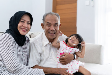 asian muslim family. portrait of happy grandparent with their granddaughter looking at camera smiling