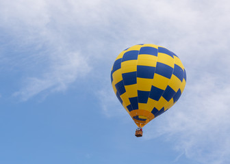 Naklejka premium A blue and yellow hot air balloon rises into a blue sky with wispy white clouds