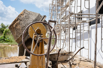 Mobile electric cement mixer and wheelbarrow in construction site.