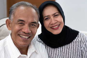 asian senior muslim couple sitting on the sofa and smiling to the camera