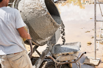 Construction worker pour cement into wheelbarrow. Cement mixer machine equipment in construction site.