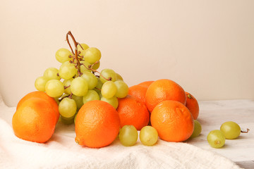 Composition of oranges, green grapes and linen cloth on wooden table. Still life of fresh fruits.