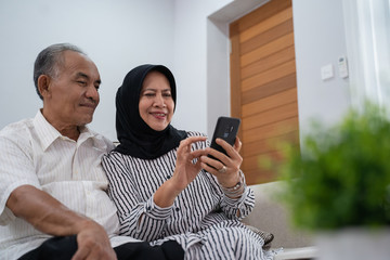 mature asian couple using modern smartphone technology at home together - obrazy, fototapety, plakaty