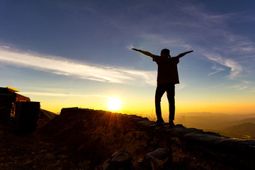 Silhouette of traveler stand exten and raise arms at top of mountain.