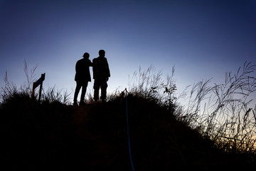 Fototapeta premium silhouette of two hikers stand at top of mountain.
