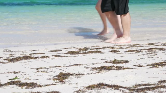 Couple walk along the beach. Closeup on people legs walking at seaside, tropical vacations