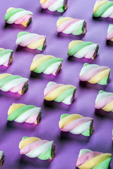 Colorful marshmallow is laid out on a purple paper background. pastel shades textured pattern