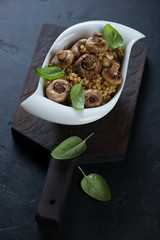 White bowl of pasta with fried mushrooms on a wooden serving board, black stone background, vertical shot