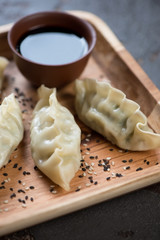 Close-up of a wooden serving tray with steamed korean dumplings and dipping sauce, selective focus