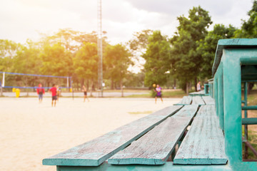 Green old wooden seat sport, stand cheer and active young volleyball players at the sand outdoor court with tree background (selective focus)