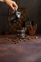 Homemade chocolate cake with liquid chocolate drops. Women's hand pours chocolate from the coffee pot