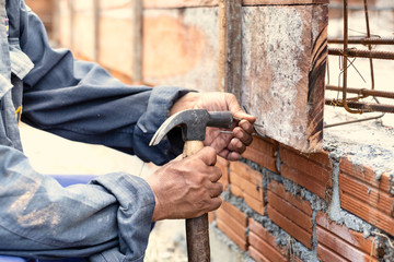 A worker using a hemmer to hit the nail for house structure in construction site, sunlight effect
