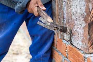 A worker is using a hammer to hit the nail for wood making ground beam for house building