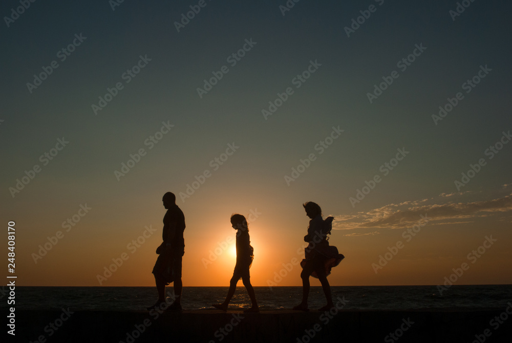 Wall mural family group of people together walking along sea shore during beautiful sunset travel