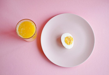 boiled egg on a pink plate and fresh orange in a glass on a pink background