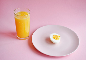 boiled egg on a pink plate and fresh orange in a glass on a pink background