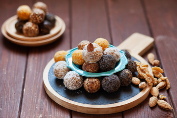 Vegan organic energy bites with nuts, chia, dates, coconut and dried fruits, healthy raw dessert snacks on wooden table