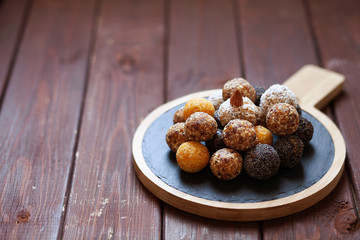 Vegan organic energy bites with nuts, chia, dates, coconut and dried fruits, healthy raw dessert snacks on wooden table