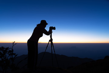 Silhouette of woman shooting with camera at sunset . Travel Concept