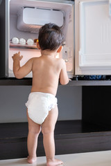Little naked baby boy looking for something in refrigerator.