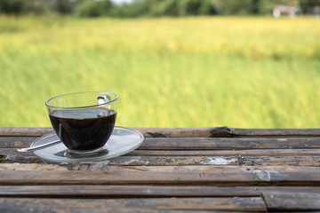 A coffee cup on bamboo floor table beside green rice field background. Green rice field view.