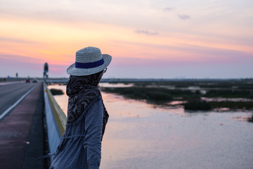 Happy muslim woman with long dress, scarf and hat standing happily at sunset. Side view.