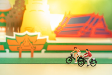 Miniature people: Group of figures cycling in front of stunning beautiful temple in Thailand using as background or tourist business concept.