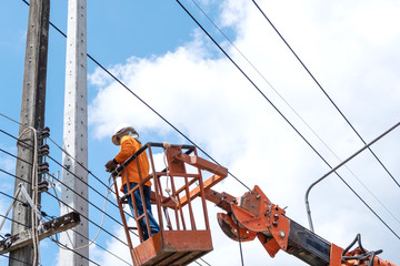 Technician works in a bucket high up on a on electric power pole.