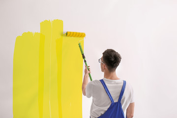 Male decorator painting wall with roller indoors