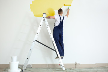 Male painter using roller for refurbishing color of wall indoors
