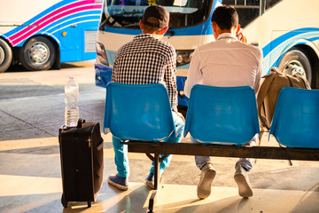 Two Thai travelers with bags sit waiting for bus in terminal at bus staion in Bangkok, Thailand.