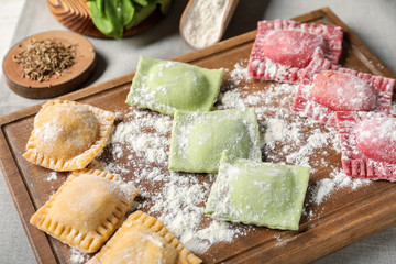 Wooden board with uncooked ravioli on table