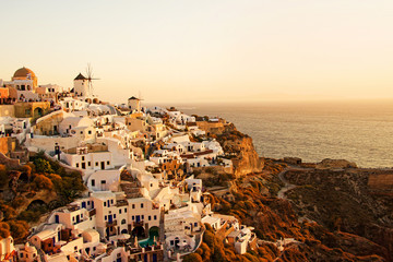 Two white old windmills on a background of white plastered houses at sunset in the town of Oia on...