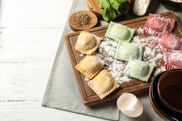 Wooden board with uncooked ravioli on table