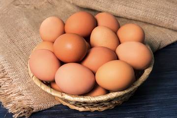 Chicken eggs in basket on a napkin of burlap on wooden table. Rustic food background
