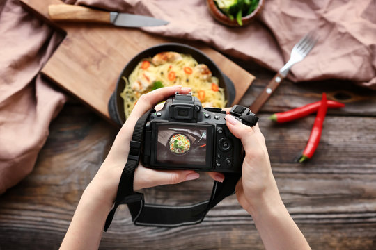 Young Woman Taking Picture Of Food On Wooden Table