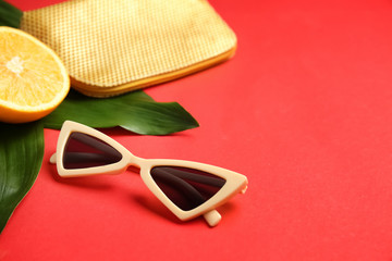 Stylish sunglasses with orange fruit, bag and tropical leaves on color background