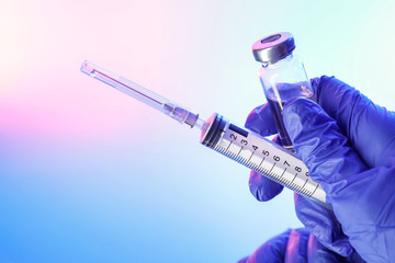 Doctor's hand with syringe and vaccine against flu on color background, closeup