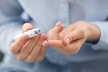 Diabetic woman taking blood sample by using lancet pen, closeup