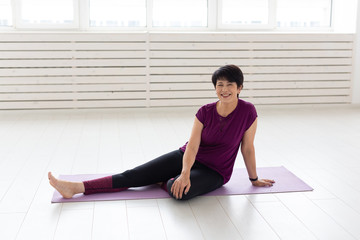 People, yoga, sport and healthcare concept - Relaxed smiling middle-aged woman sitting on exercise mat over white background