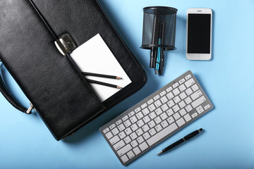 Leather briefcase with mobile phone, keyboard and stationery on color background