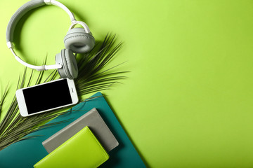 Mobile phone with headphones and stationery on color background